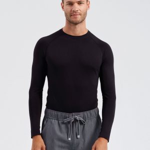 A man is standing in the image, dressed in a black t-shirt and grey pants. He is smiling and posing for the camera. The background is white.