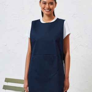 A woman is standing in the image, dressed in a blue dress and black pants. She is smiling and posing for the camera. The background features a white wall.