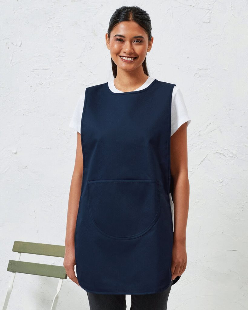 A woman is standing in the image, dressed in a blue dress and black pants. She is smiling and posing for the camera. The background features a white wall.