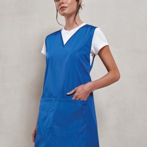 A woman is standing in the image, dressed in a blue tunic, with a white t-shirt and black pants. The background is a white wall.