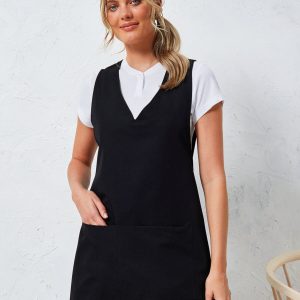 A woman is standing in the image, dressed in a black tunic, with a white shirt and jeans. The background is white, and a wooden chair is visible on the right side of the image.