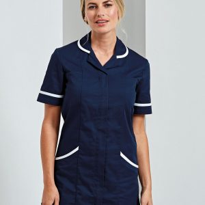 A woman is standing in the image, dressed in a blue tunic with white lines. The background is white, and the image appears to have been taken in a hall.