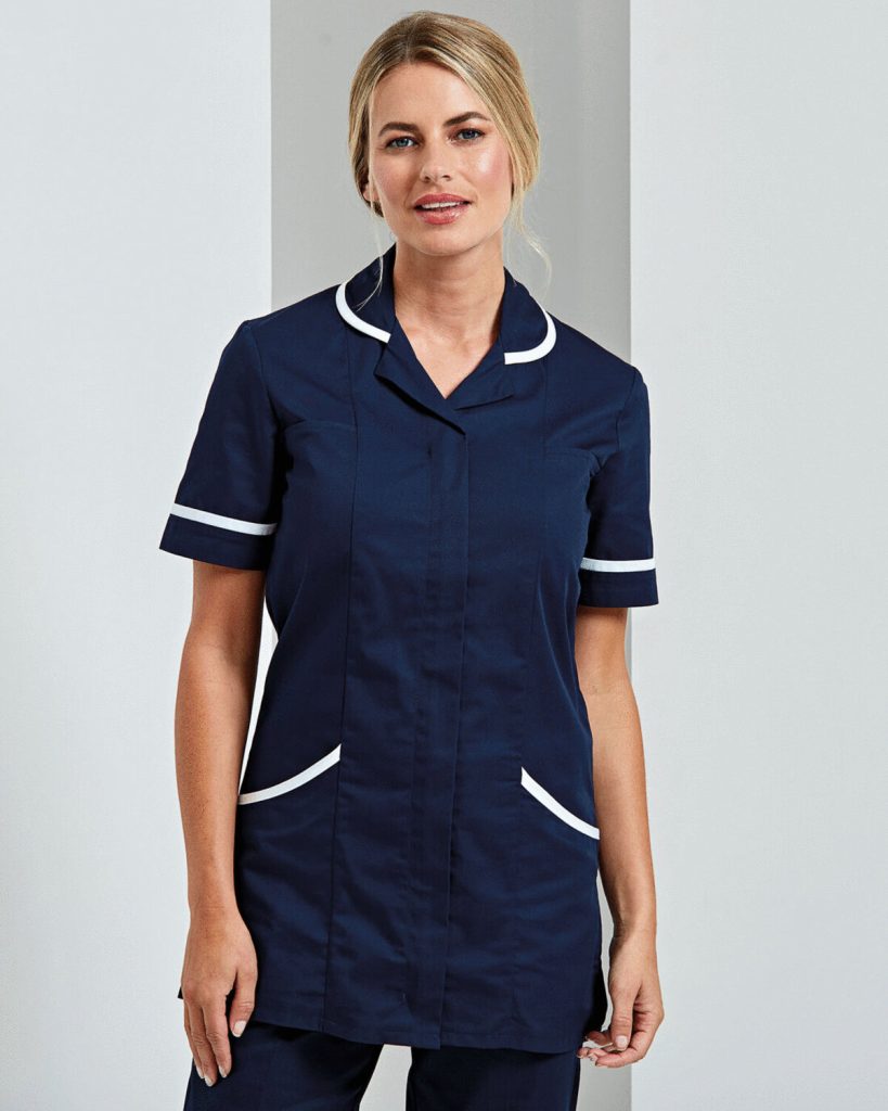 A woman is standing in the image, dressed in a blue tunic with white lines. The background is white, and the image appears to have been taken in a hall.