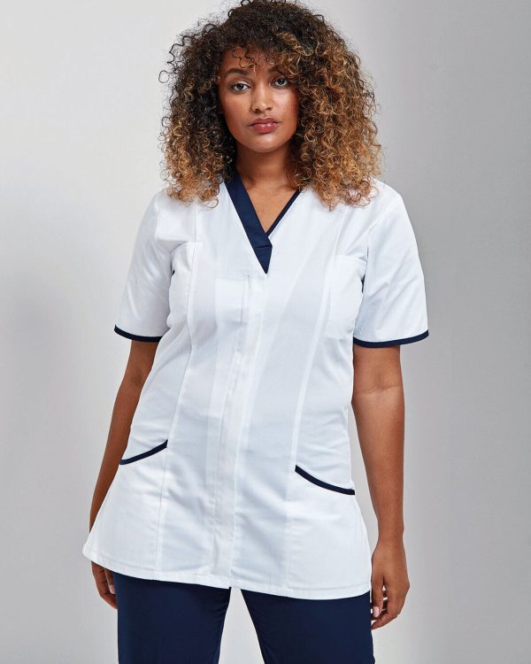 A woman is standing in the image, dressed in a white tunic with blue accents. She is wearing a black top and blue pants. The background is white.