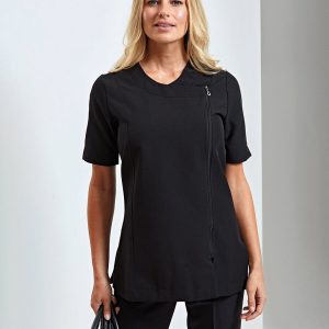 A woman is standing in the image, dressed in black. She is holding a brush in her hand and smiling. The background is white.